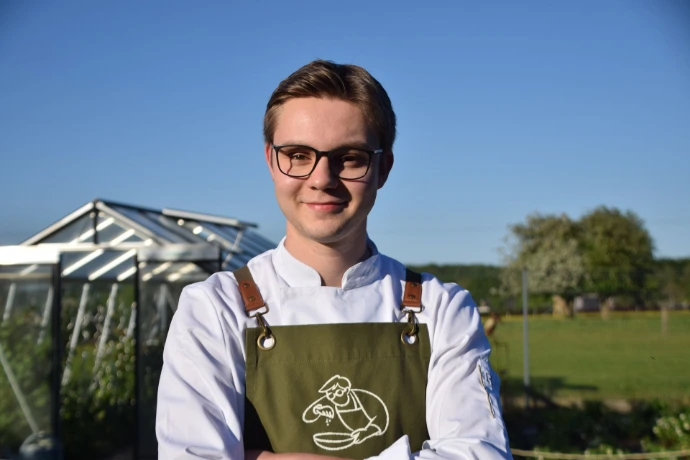 Florent Maldague, chef privé, en veste de cuisine et tablier vert devant une serre