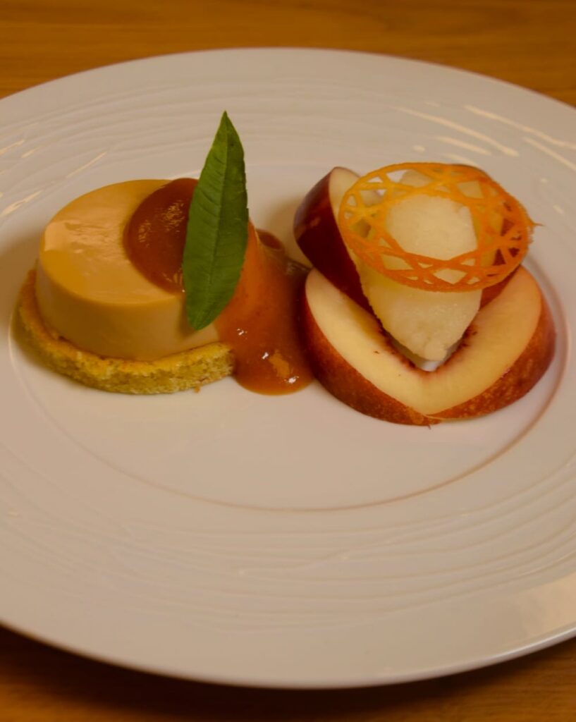 Dessert de saison : panna cotta caramel et pêche, dressés sur une assiette blanche