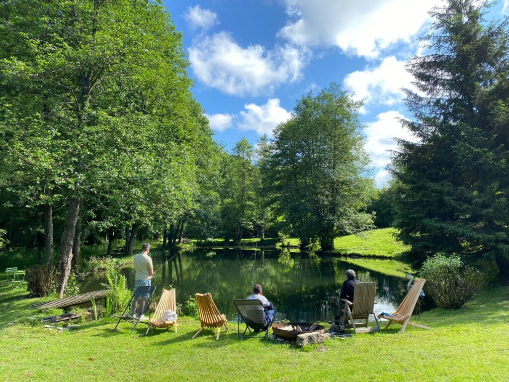 Pêche à la truite - Trois pêcheurs au bord de l'étang privé du gîte de Liresse, entre fauteuils en bois et brasero, sous les arbres