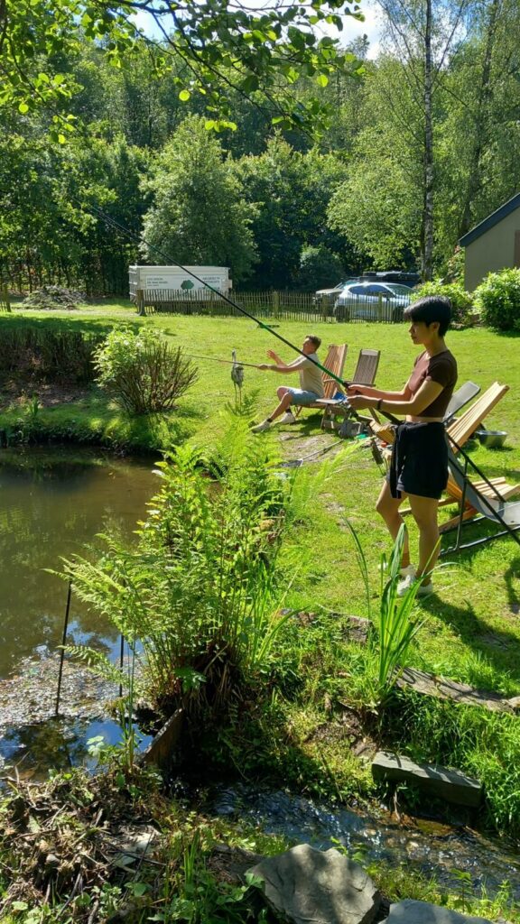 Deux pêcheurs avec leurs cannes au bord de l'étang du gîte de Liresse, installés sur des fauteuils en bois dans l'herbe